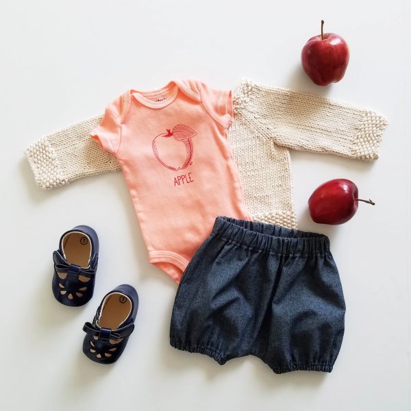 hand dyed, screen printed red apple bodysuit flatlay with indigo denim bloomers and natural sweater